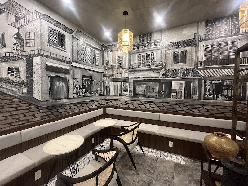Cushioned bench seating and marble tables under the painted shophouse mural